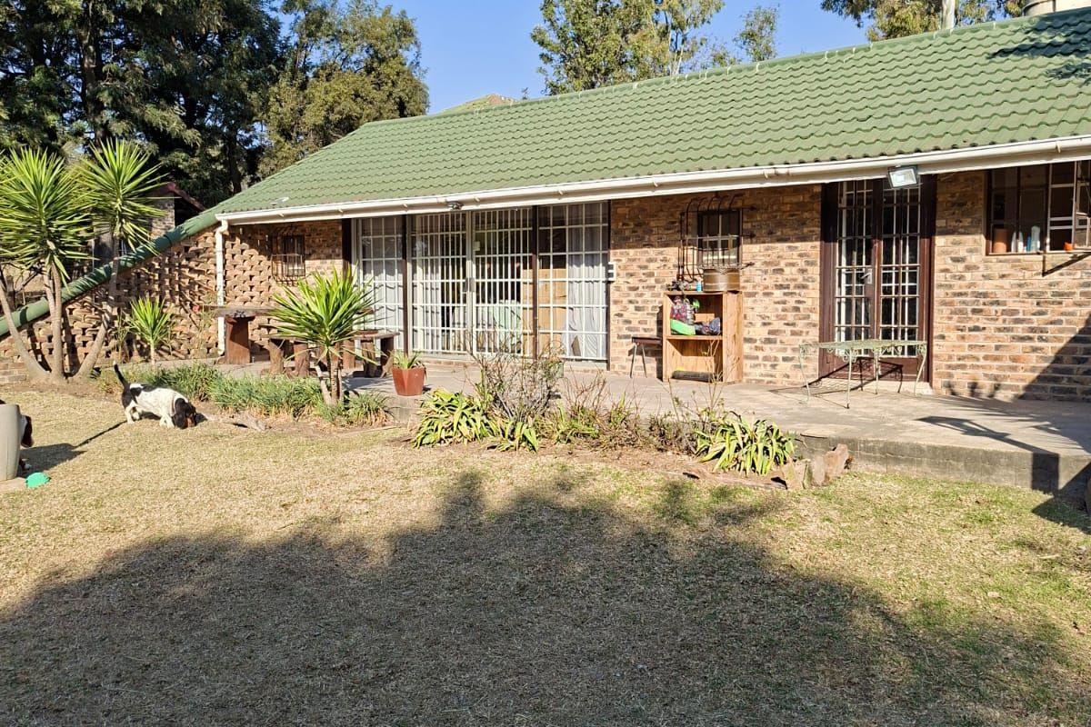 Rear view of a single-story brick house featuring a tiled roof, concrete patio area, and sliding glass doors with security gates.