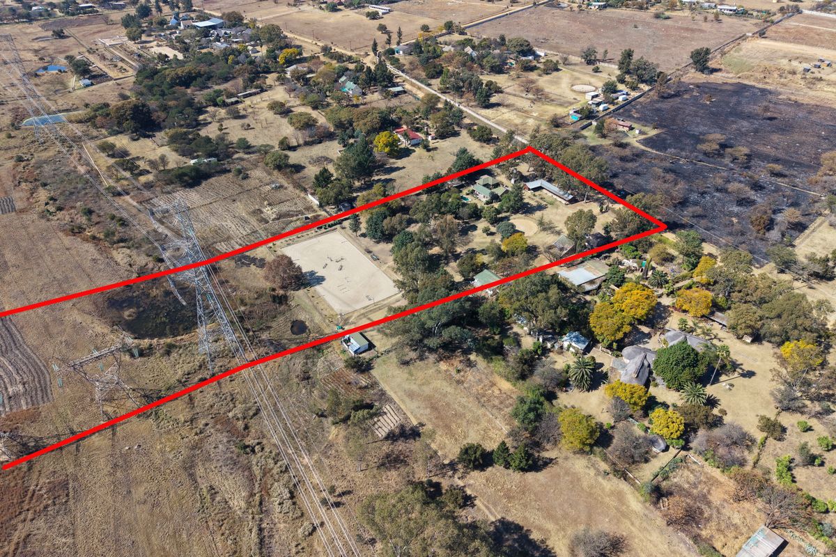 Aerial view of a large rural property featuring an equestrian arena, multiple outbuildings, and extensive grounds surrounded by natural landscape.