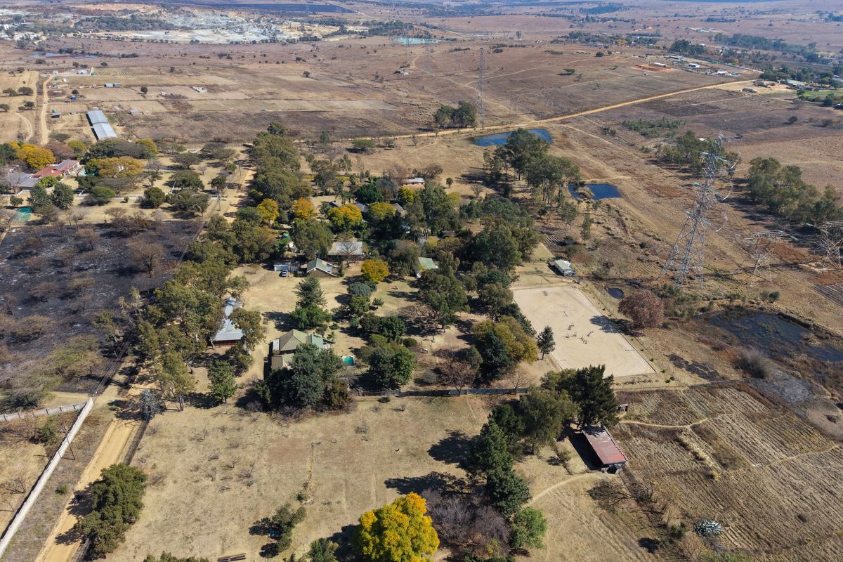 Aerial view of a large rural property featuring mature trees, open land, a sand arena, and multiple outbuildings set within a vast landscape.
