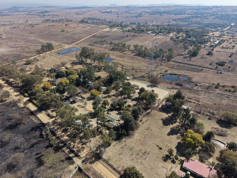 Aerial view of a rural property featuring multiple structures, mature trees, a swimming pool, and surrounding open landscape.