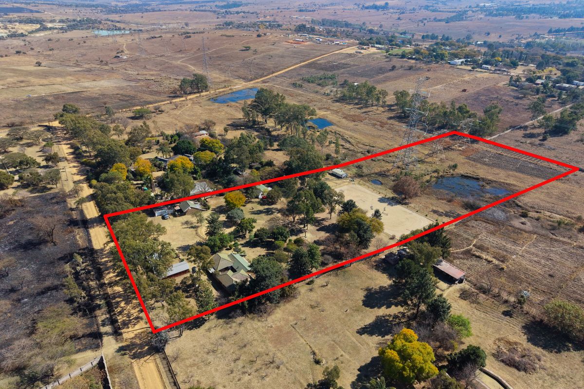 Aerial view of a large rural property plot with established trees, outbuildings, and surrounding landscape, highlighted by a red boundary outline.