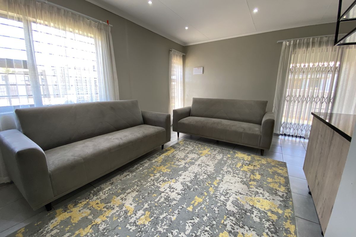 A bright and well-maintained living room featuring neutral wall tones, tiled flooring, recessed downlighting, and secure window and door access.