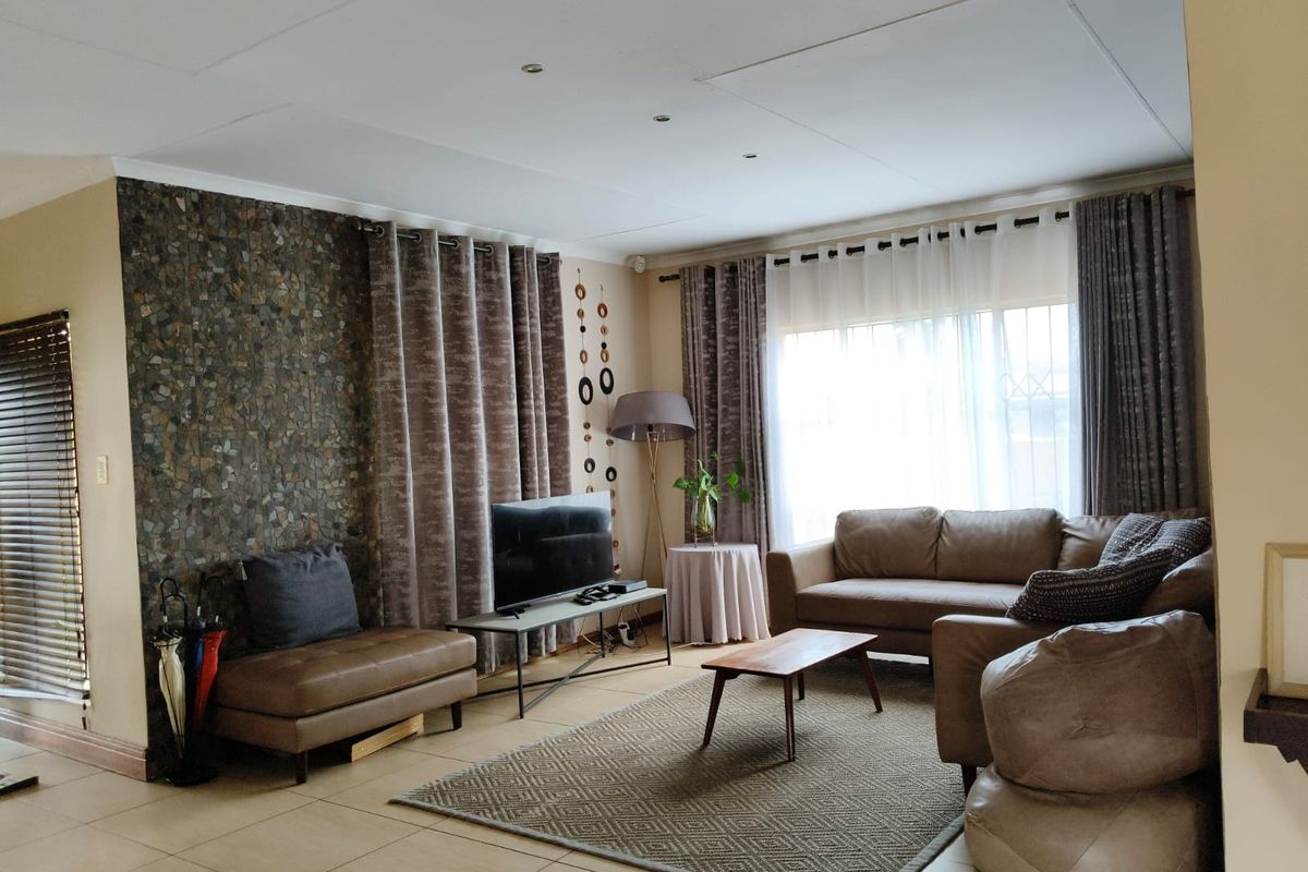 A comfortable living room featuring a textured stone accent wall, tiled flooring, and large windows that provide ample natural light.