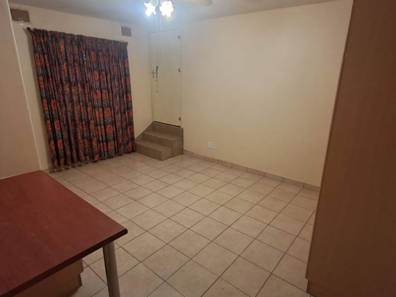 A spacious bedroom featuring tiled flooring, a ceiling fan, and built-in storage, offering a blank canvas for potential interior updates.