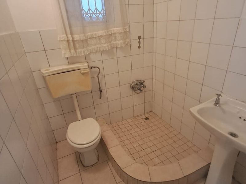 A dated bathroom featuring a pedestal basin, toilet, and a raised shower base with full-height wall tiling.