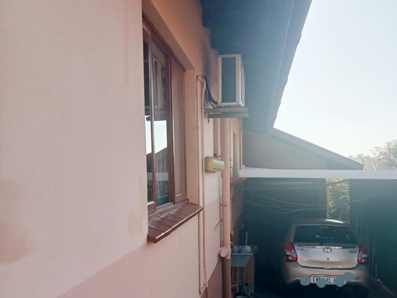 Side view of the cottage showing exterior wall, window, mounted air conditioning unit, and a covered carport area.