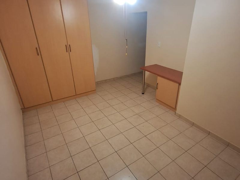 A functional bedroom featuring tiled flooring, built-in cupboards, a built-in desk, and a ceiling fan, offering a clean and versatile space.