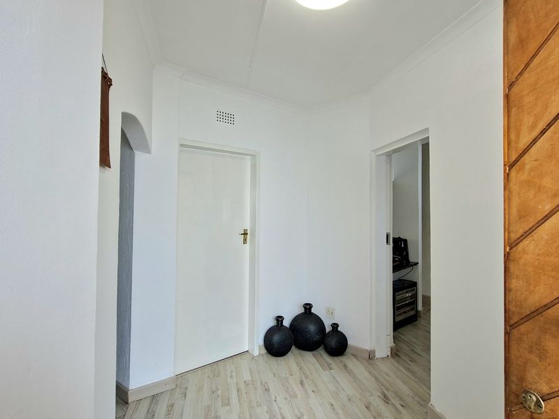 A bright and clean hallway featuring light-toned laminate flooring, coved ceilings, and an arched transition leading to adjacent living spaces.