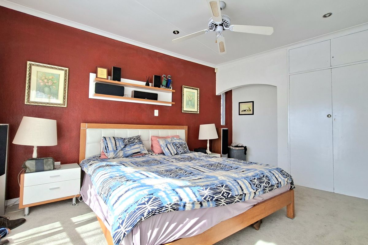 A spacious bedroom featuring built-in cupboards, a ceiling fan, and a distinct red accent wall with integrated shelving.