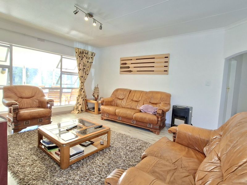 A bright living room featuring large windows, laminate flooring, and track lighting, offering a comfortable and well-lit space for relaxation.