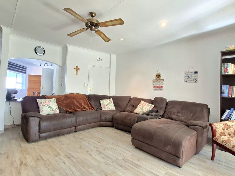 A spacious living room featuring light-toned laminate flooring, a ceiling fan, and an open archway leading to an adjacent area.