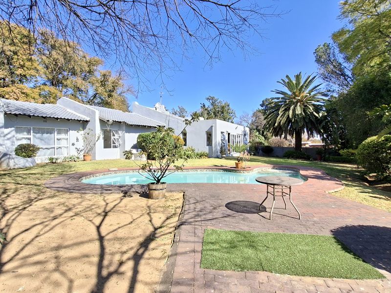 Rear view of the property featuring a swimming pool, brick paved patio area, and established garden surroundings.