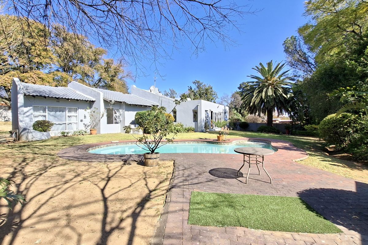 Rear view of the property featuring a swimming pool, brick paved patio area, and established garden surroundings.