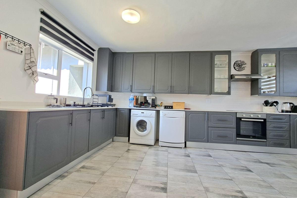 Modern kitchen featuring grey shaker-style cabinetry, white stone countertops, built-in oven, extractor fan, and tiled flooring.