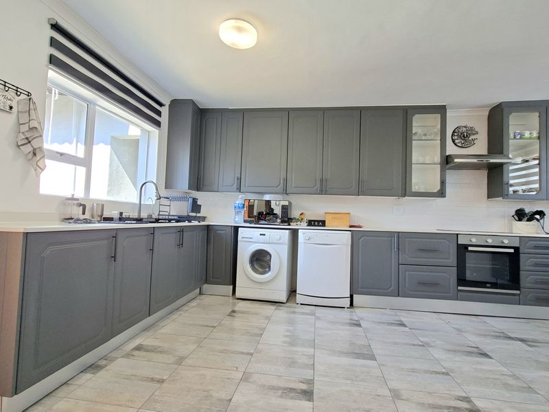 Modern kitchen featuring grey shaker-style cabinetry, white stone countertops, built-in oven, extractor fan, and tiled flooring.