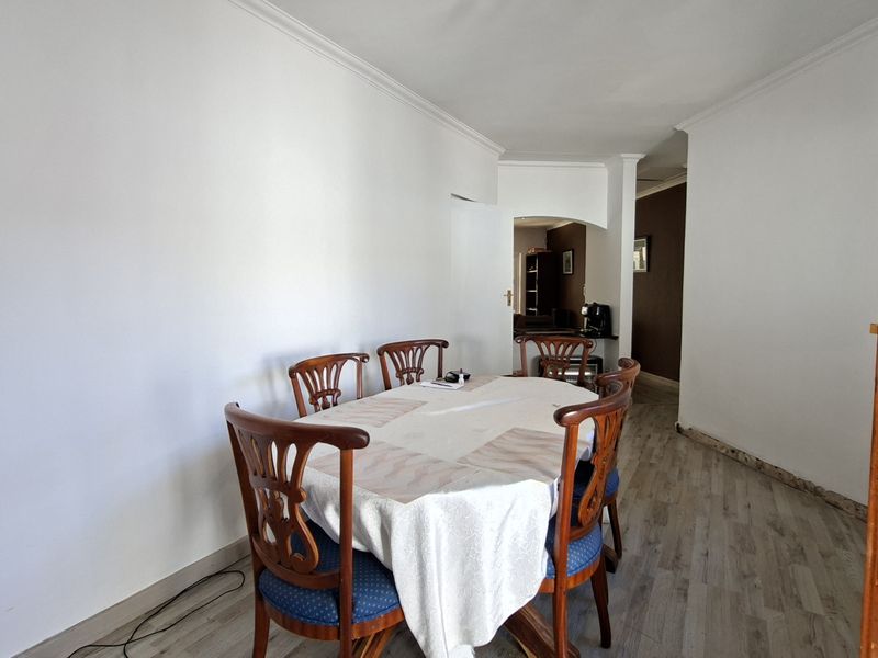 Dining area featuring laminate flooring and coved cornicing, leading through an archway to an adjacent room. Note the unfinished skirting boards at the wall base.