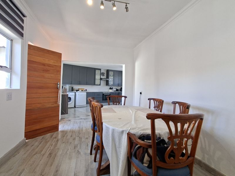 Open-plan dining area flowing into a modern kitchen with dark cabinetry, featuring wood-look tile flooring and neutral wall finishes.