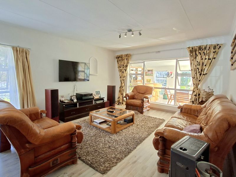 A spacious living room featuring light-toned laminate flooring, large windows providing natural light, and direct access to an outdoor patio area.