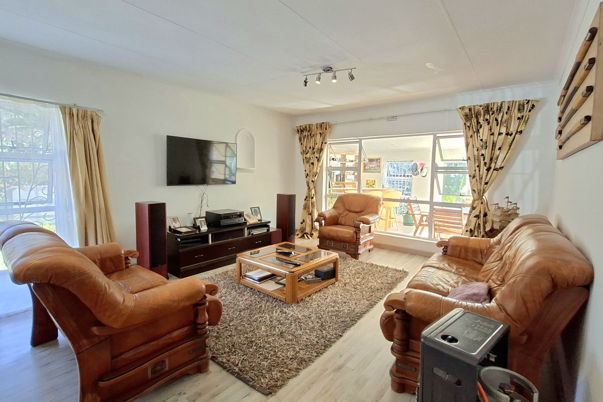A spacious living room featuring light-toned laminate flooring, large windows providing natural light, and direct access to an outdoor patio area.