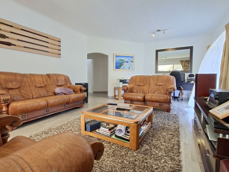 A spacious living room featuring light-toned laminate flooring, neutral walls, and an arched entryway leading to adjacent areas of the home.