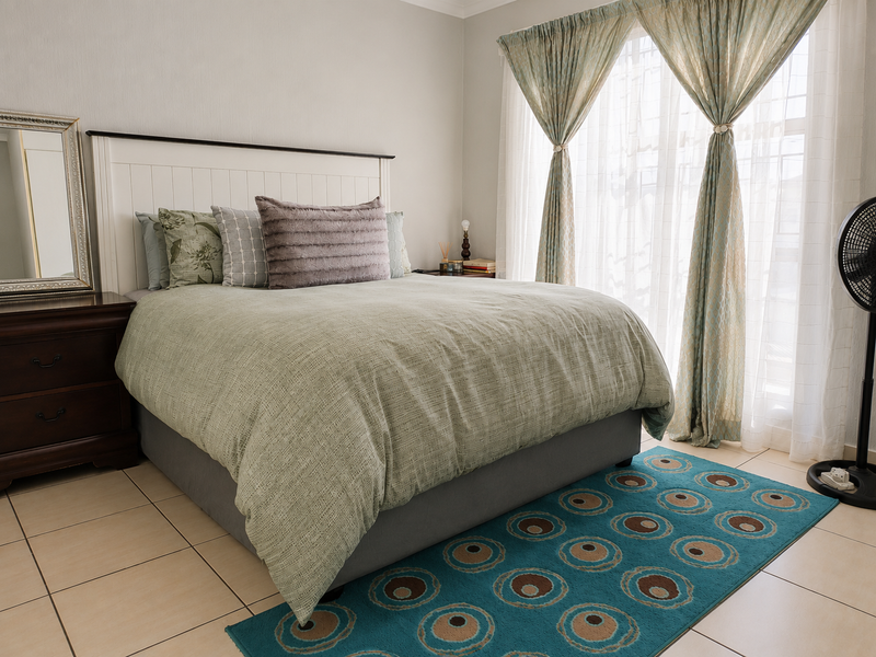 A well-maintained bedroom featuring neutral wall tones, tiled flooring, and large windows with installed curtain tracks.