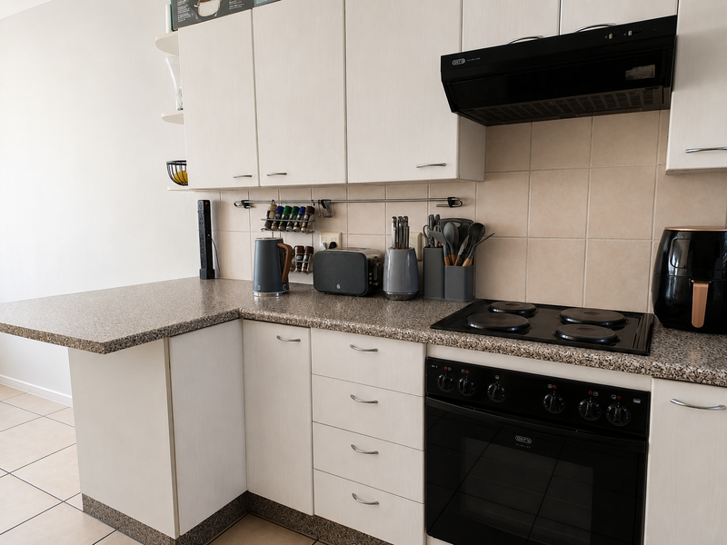 A functional kitchen featuring light-toned cabinetry, laminate countertops, a built-in oven with an electric hob, and a tiled backsplash.
