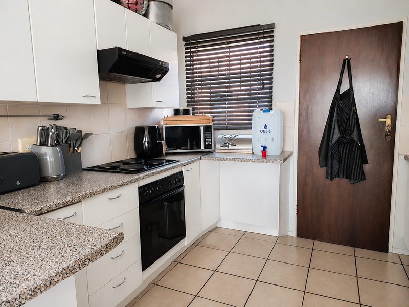 A functional kitchen featuring white cabinetry, granite-look laminate countertops, built-in oven and hob, extractor fan, and tiled flooring.