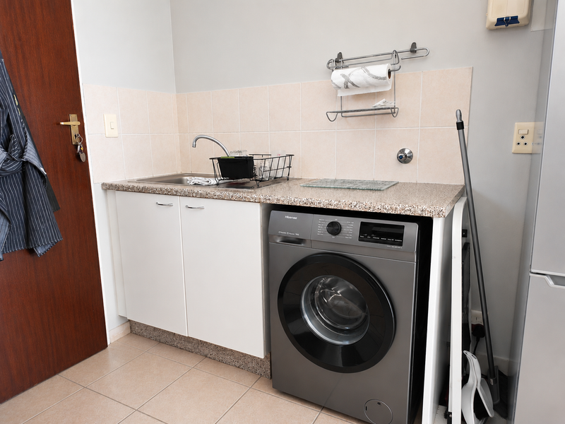 A functional laundry area featuring a stainless steel sink, laminate countertop, built-in cabinetry, and tiled backsplash.