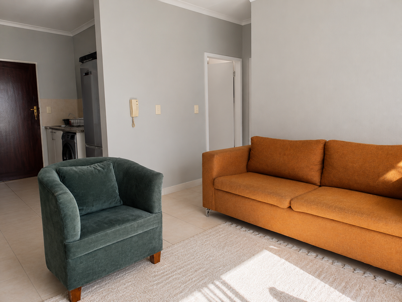 Open-plan living area featuring tiled flooring, neutral wall tones, and a compact kitchen space visible in the background.