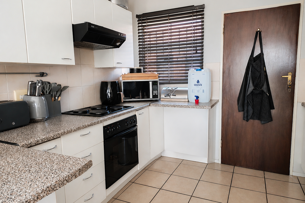 A functional kitchen featuring white cabinetry, granite-look laminate countertops, built-in oven and hob, extractor fan, and tiled flooring.