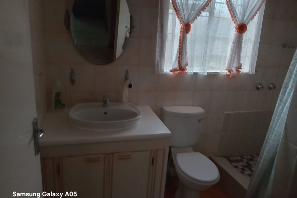 A dated bathroom featuring a vanity cabinet with a basin, a standard toilet, and a shower area with wall tiling.
