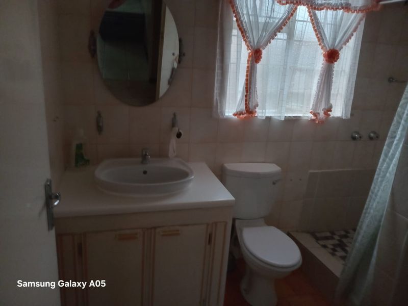 A dated bathroom featuring a vanity cabinet with a basin, a standard toilet, and a shower area with wall tiling.