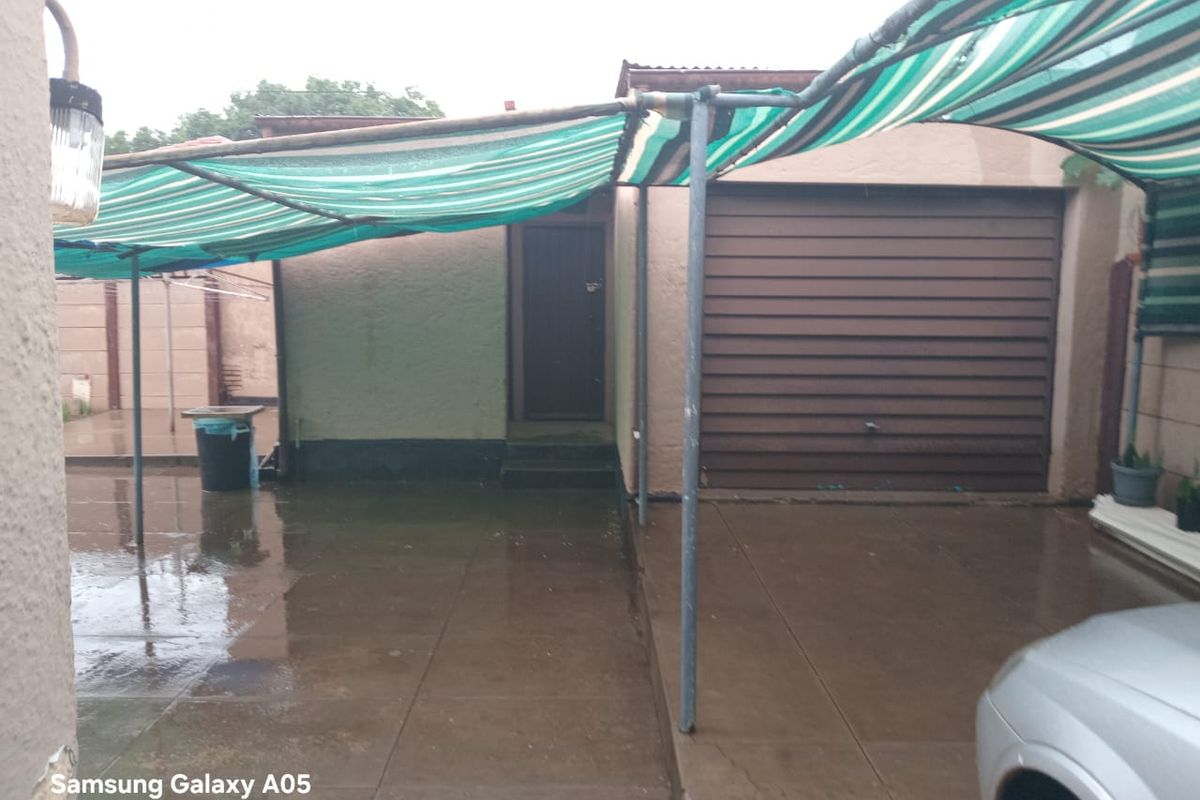 Rear exterior area featuring a paved patio, a garage entrance, and a shade cloth structure covering the outdoor space.
