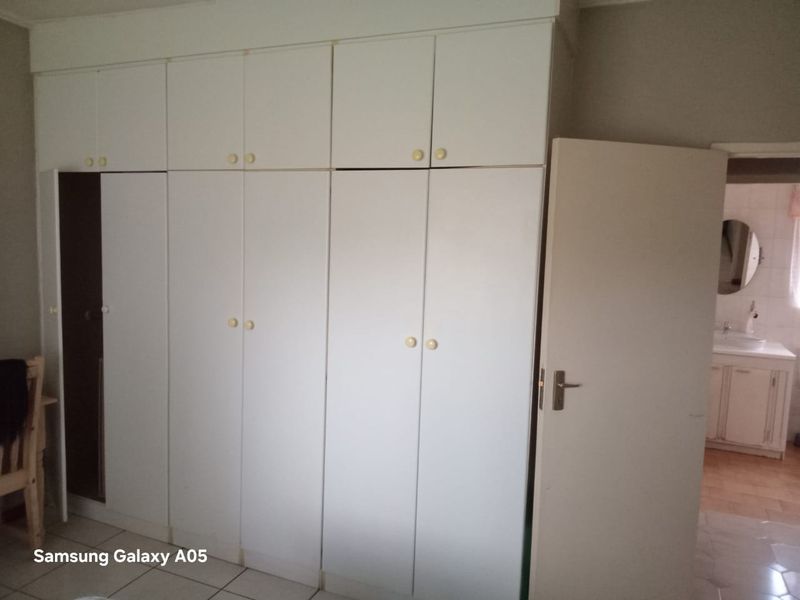A bedroom featuring extensive white built-in cupboards and tiled flooring, with an adjacent view into a bathroom area.