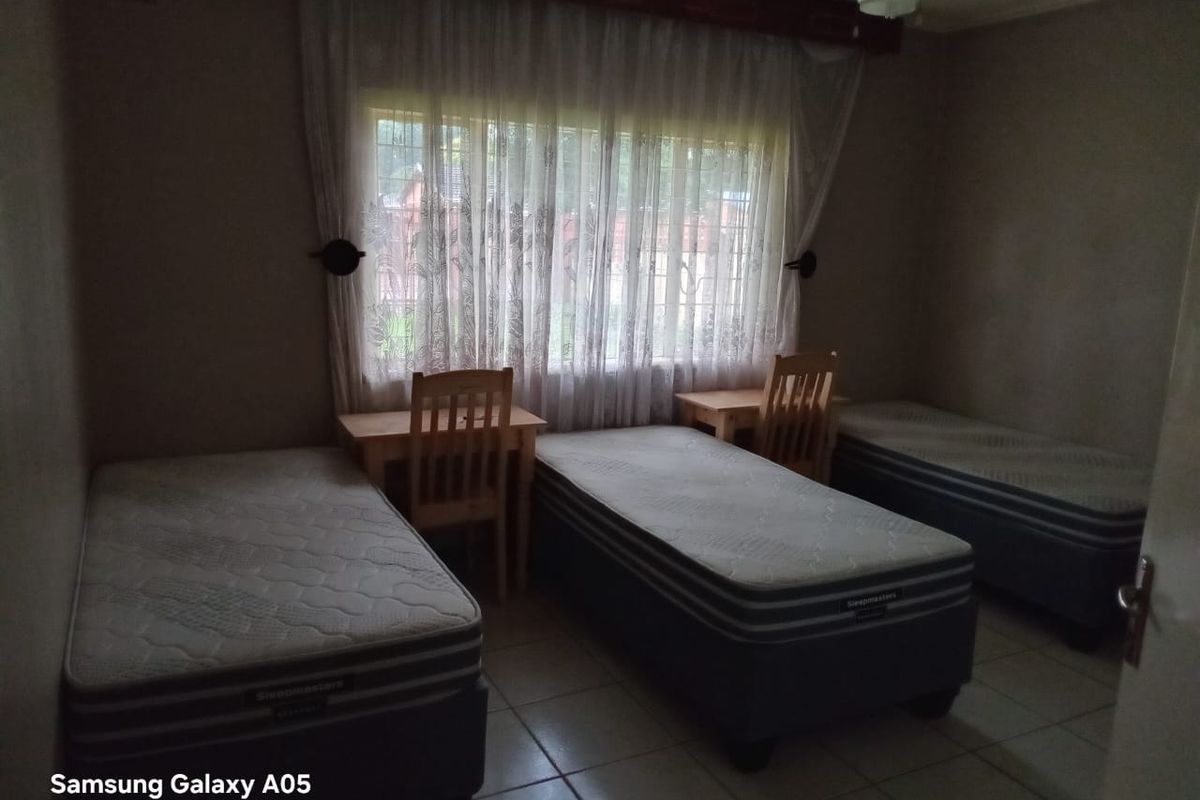 A functional bedroom featuring tiled flooring, a ceiling fan, and security bars on the window, providing a practical space for multiple occupants.