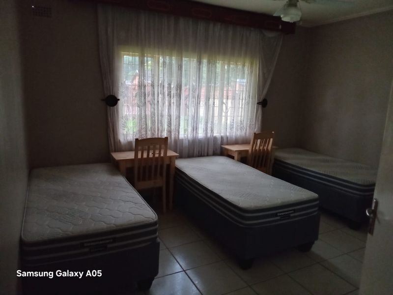 A functional bedroom featuring tiled flooring, a ceiling fan, and security bars on the window, providing a practical space for multiple occupants.