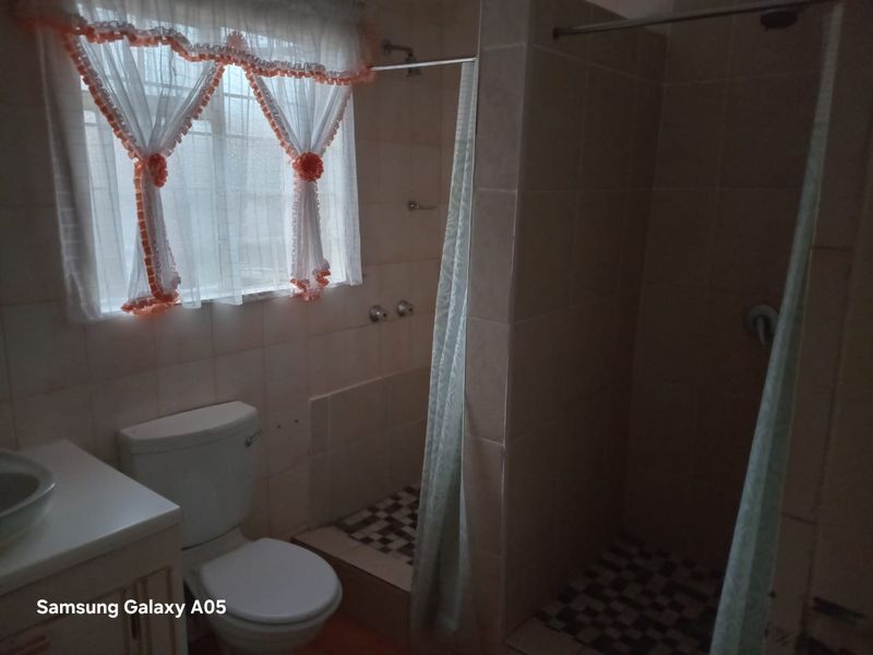 A functional bathroom featuring a shower enclosure, toilet, and vanity basin with tiled finishes throughout.