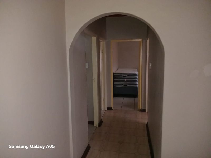 A simple interior hallway featuring an arched entryway and tiled flooring, providing access to adjacent rooms.
