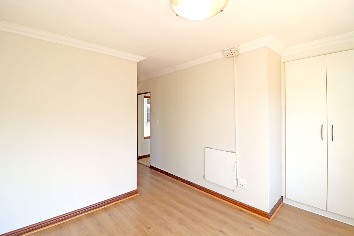 A bright, empty bedroom featuring laminate flooring, built-in wardrobe storage, and a wall-mounted heater.