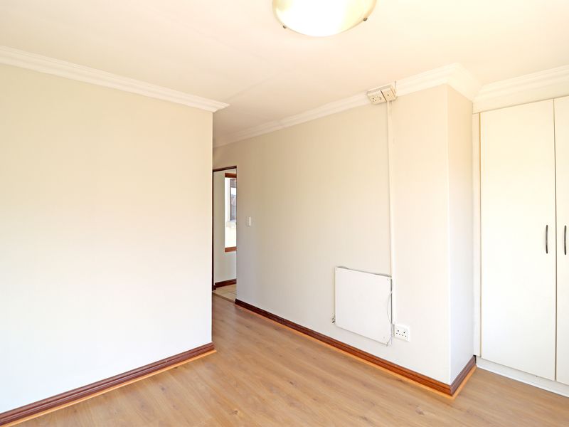 A bright, empty bedroom featuring laminate flooring, built-in wardrobe storage, and a wall-mounted heater.