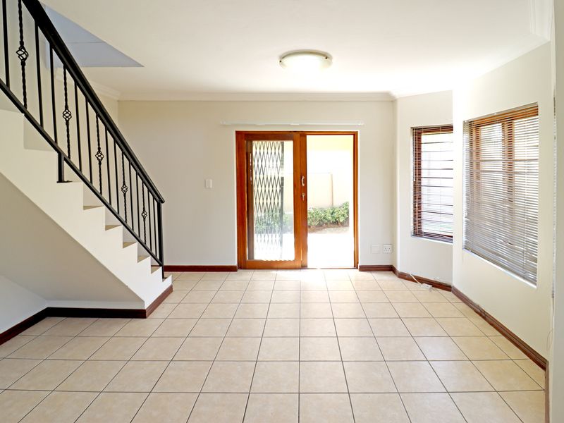 A bright, open-plan living area featuring neutral tiled flooring, a staircase with wrought iron railing, and direct access to the outdoor space.
