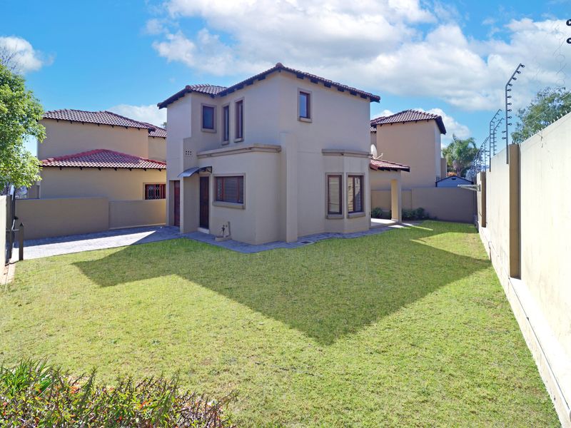 A view of the rear exterior of the house featuring a well-maintained lawn, paved driveway, and secure boundary walls with electric fencing.