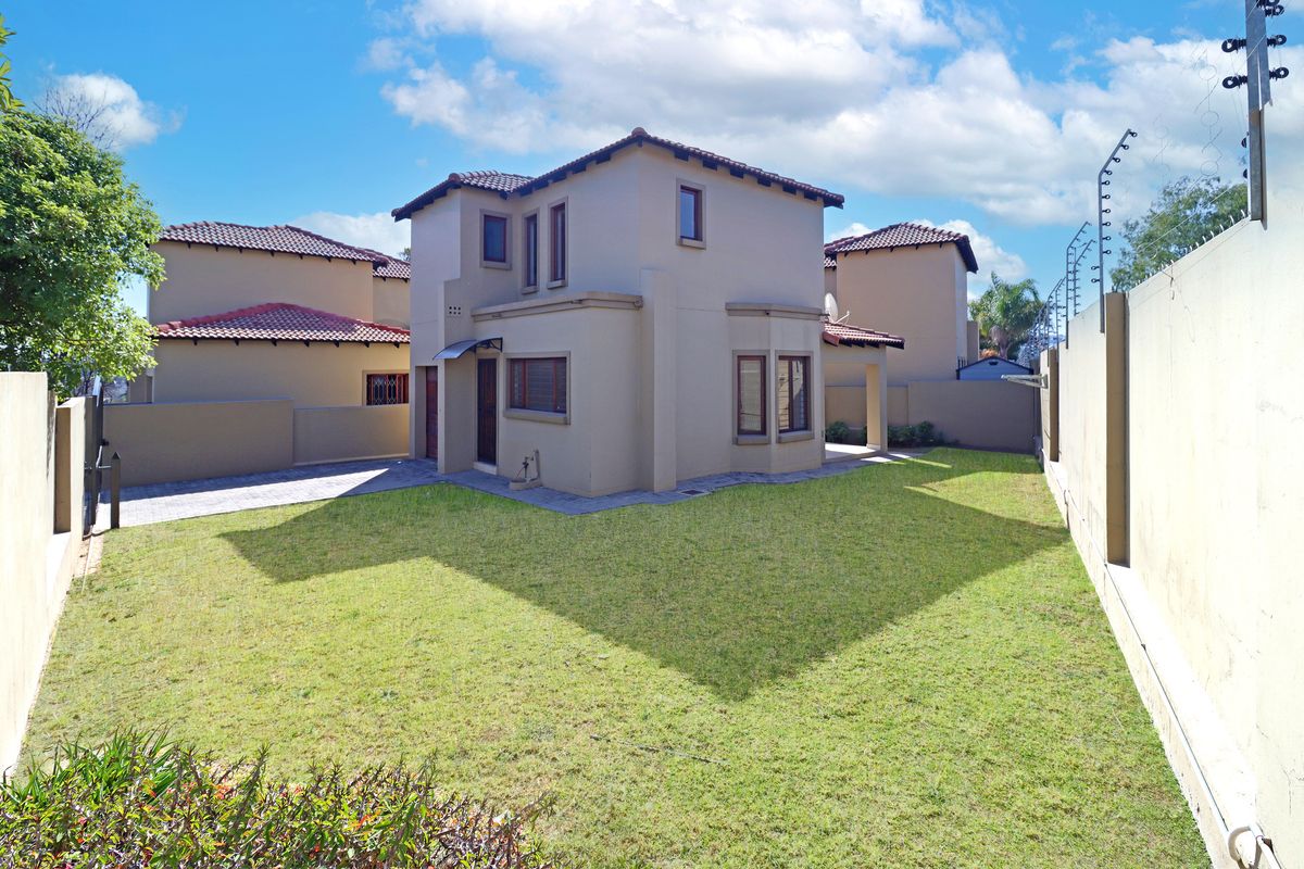 A view of the rear exterior of the house featuring a well-maintained lawn, paved driveway, and secure boundary walls with electric fencing.