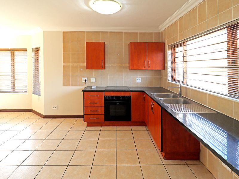 A clean, empty kitchen featuring wooden cabinetry, dark granite countertops, a built-in oven and hob, and tiled flooring with ample natural light.