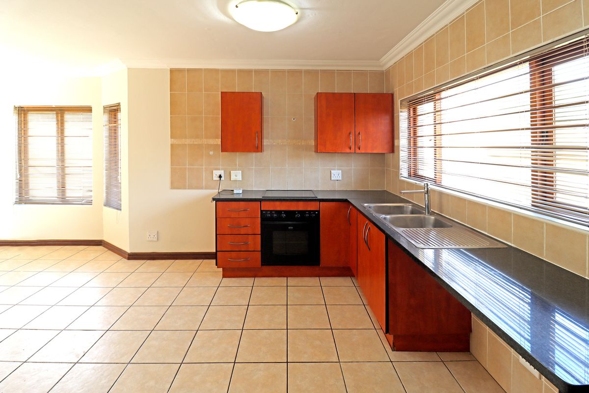 A clean, empty kitchen featuring wooden cabinetry, dark granite countertops, a built-in oven and hob, and tiled flooring with ample natural light.