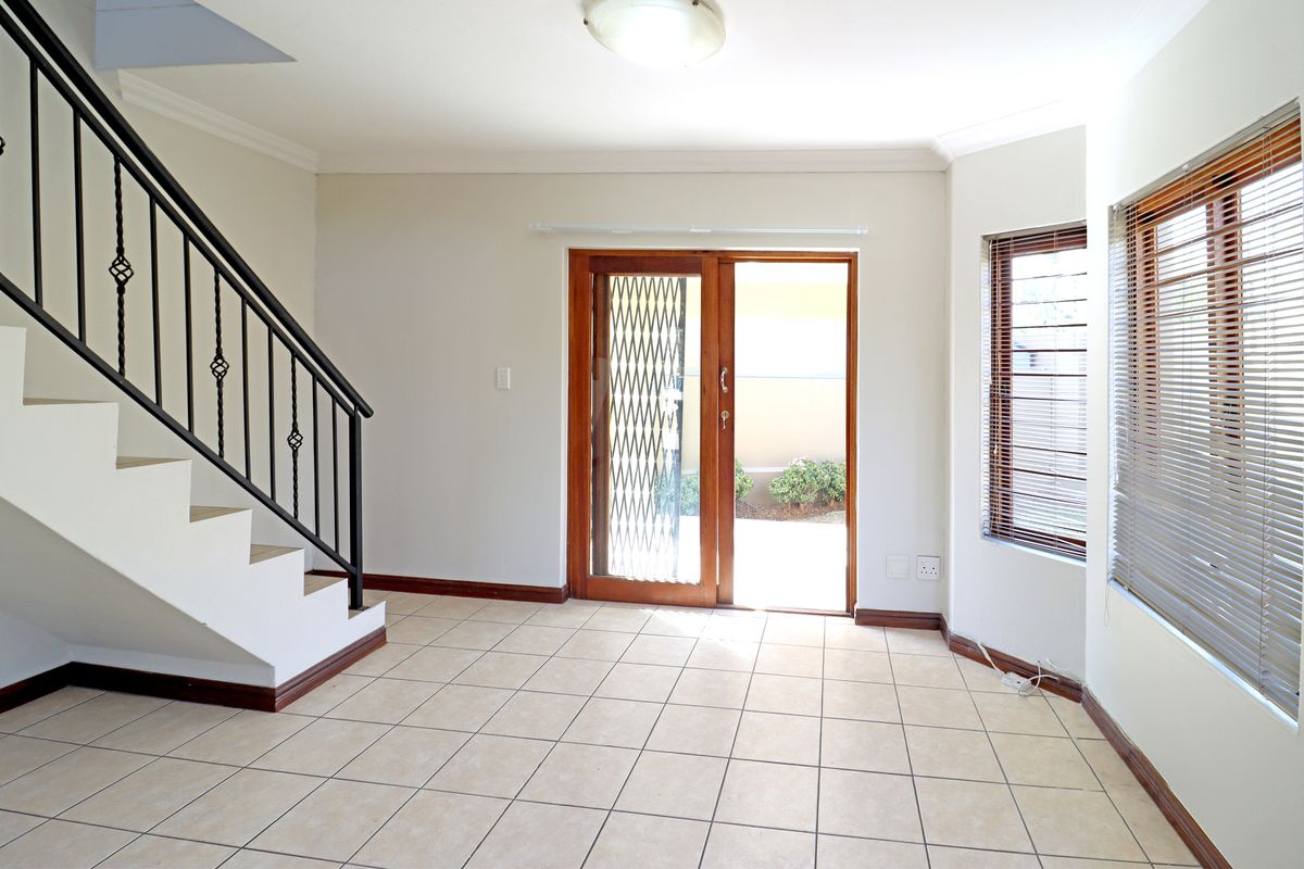 Bright and spacious living area featuring tiled flooring, a staircase with a wrought iron balustrade, and sliding glass doors leading to the exterior.