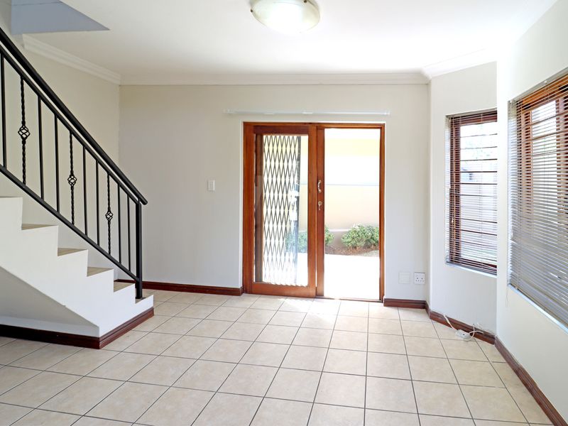 Bright and spacious living area featuring tiled flooring, a staircase with a wrought iron balustrade, and sliding glass doors leading to the exterior.