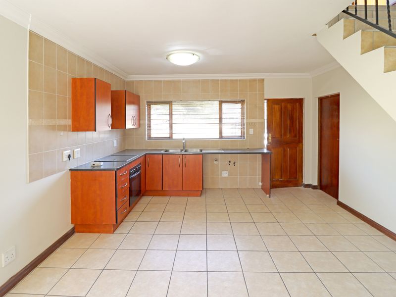 A functional kitchen featuring built-in cabinetry, tiled flooring, and a tiled backsplash, situated beneath an internal staircase.