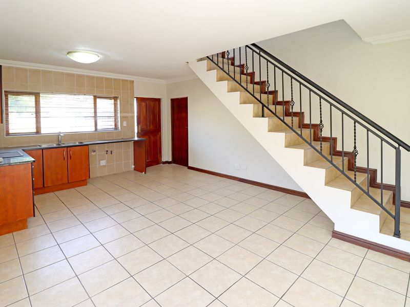 An open-plan living and kitchen area featuring tiled flooring, built-in cabinetry, and a staircase with a metal balustrade.