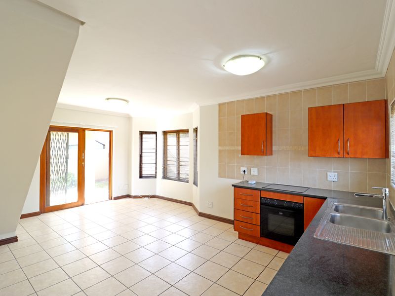 Spacious open-plan kitchen and living area featuring tiled flooring, built-in cabinetry, integrated oven and hob, and direct access to the exterior via sliding doors.